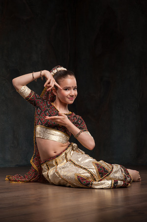 schoolgirl learns Indian dance. Sitting on a stone and repeats the motion, dressed in traditional costumeの写真素材