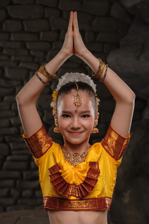 European child in national costume of India. Keeps hands collected over his head and smiles