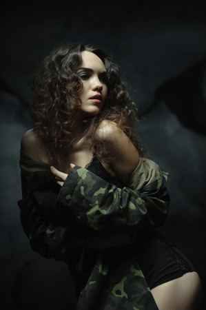 beautiful young brunette in military clothing. posing for the camera. Grey stones in the backgroundの写真素材