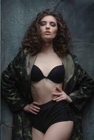 Beautiful young woman in black lingerie, dressed in a military coatの写真素材