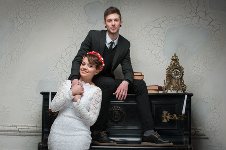 young beautiful couple posing for the camera near the piano. guy sits in the center of the frameの写真素材