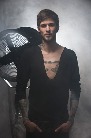 silhouette of a guy in tight pants in front of a big ventilator. Man with tattoos , holding both hands in his pocketsの写真素材
