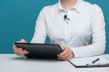 Close up portrait of hands of elegant woman reporter holding the notebook and sitting at the table. There are also pen and folder lying on the table, isolated on a blue background and there is copy place in the left sideの写真素材