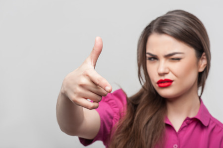 Waist up portrait of beautiful girl reporter, who is looking at the camera and raising her right hand in such way as if she were trying to shoot someone, her left eye is closed and she has brown hair and red lips, isolated on a grey background and there iの写真素材