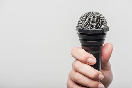 Close up portrait of microphone, which woman reporter is holding, proposing someone to answer her questions and waiting for the answer, isolated on a grey background and there is copy place in the left sideの写真素材