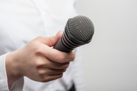 Close up portrait of microphone, which is hold by woman tv reporter and visible on the foreground. The girl is waiting for the answer of someone and the figure of her is slightly blurred, isolated on a grey background and there is copy place in the right の写真素材
