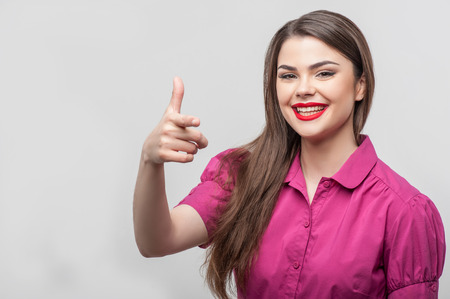 Waist up portrait of beautiful girl reporter with Caucasian appearance, who is smiling and looking at the camera and raising her right hand in such way as if she were trying to shoot someone in jest, isolated on a grey background and there is copy place iの写真素材