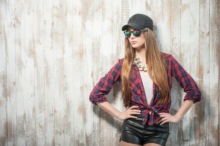 Waist up portrait of beautiful hipster girl with cap and sunglasses, who is standing arms akimbo seriously looking towards, isolated on a white background and there is copy place in the left sideの写真素材