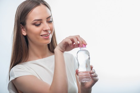 beautiful girl is holding the bottle of water with pretty smile. She is looking at it and opening it. isolated on a white backgroundの写真素材