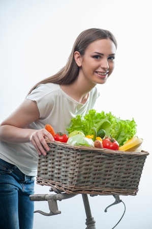 Waist up portrait of healthy beautiful girl with basket of healthy fruits and vegetables. isolated on a white backgroundの写真素材