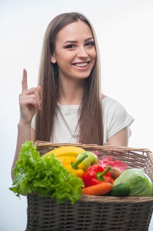 Waist up portrait of beautiful woman suggesting to eat healthy food. She is holding the basket of vegetarian food and smiling. isolated on a white backgroundの写真素材