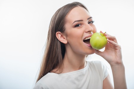 Waist up portrait of pretty girl, who is biting an apple with appetite. isolated on a white backgroundの写真素材