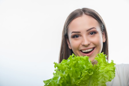 Waist up portrait of beautiful girl holding leaves of a salad with big enjoyment. isolated on a white backgroundの写真素材