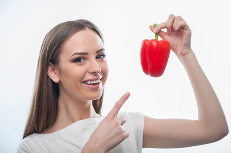 beautiful woman is pointing her finger on the pepper. She is holding it in her hand while smiling happily, isolated on a white backgroundの写真素材