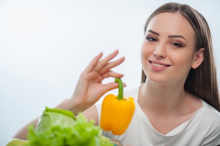 Beautiful woman is showing yellow pepper to the camera. Isolated on a white backgroundの写真素材