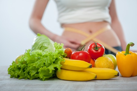 Close up of vegetables and fruits on the table. The girl is standing behind it and takes measurements of her waistの写真素材