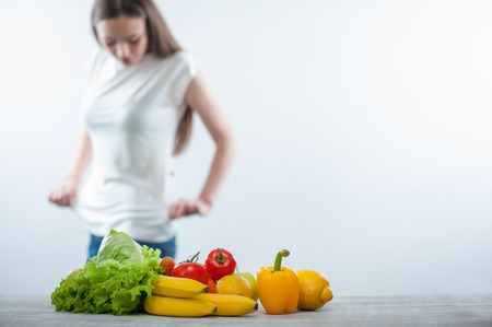 Cheerful healthy woman is sighting herself carefully. Focus on healthy food. Isolated on a white backgroundの写真素材