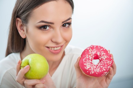 Cheerful woman is showing to the camera apple and donut. Isolated on a white backgroundの写真素材