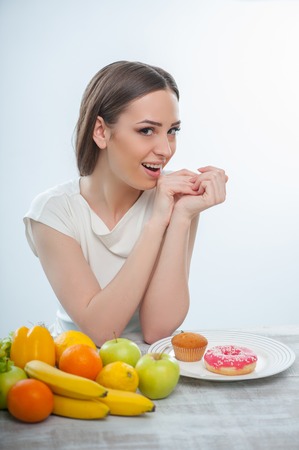 Beautiful girl wants to eat fruits and donuts. Isolated on a white backgroundの写真素材