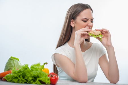 Pretty woman is biting harmful hamburger with disgust. Isolated on a white backgroundの写真素材