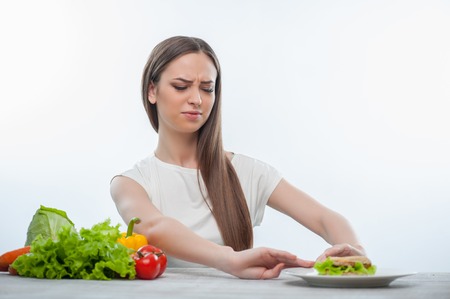 Pretty woman is refusing to eat unhealthy hamburger. Isolated on a white backgroundの写真素材