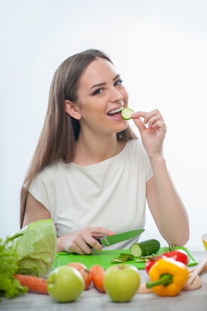 beautiful woman is testing fresh cucumber with pleasure. isolated on a white backgroundの写真素材