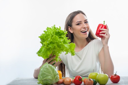 pretty girl is sitting at the table and presenting leaves of salad and a red pepper. isolated on white backgroundの写真素材