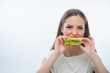Hungry pretty woman is biting hamburger gradually. Isolated on a white backgroundの写真素材
