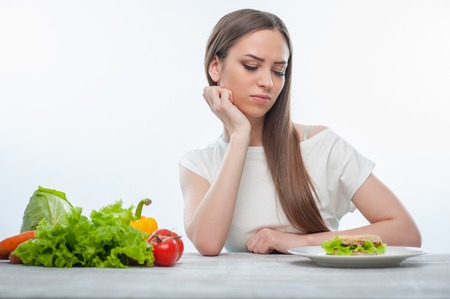 Beautiful girl is looking at hamburger with aversion. Isolated on a white backgroundの写真素材