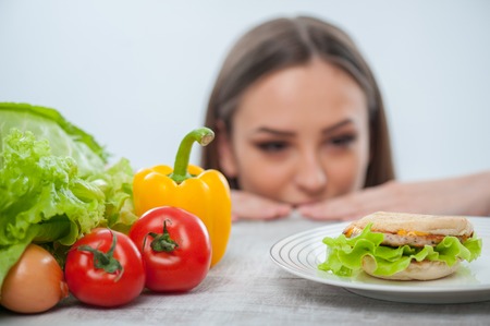 Beautiful young girl is looking at the hamburger with appetite. Focus on hamburger and vegetables, Isolated on a white backgroundの写真素材
