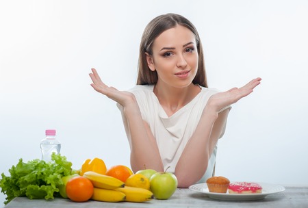 Pretty woman cannot make a decision what she should eat. Isolated on a white backgroundの写真素材