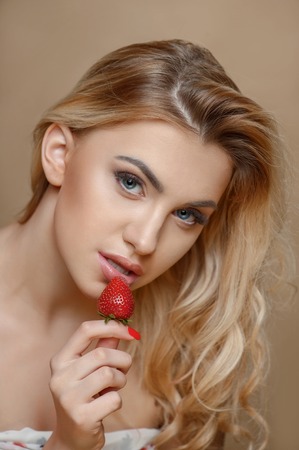 Cheerful woman is eating strawberry with desire. She is expressing her sexuality. Isolated on brown backgroundの写真素材