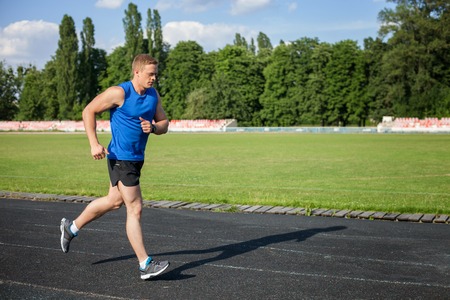 Handsome sportsman is running towards track in stadium. He is looking forward with concentration....