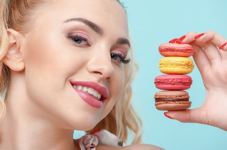 Beautiful woman is showing appetite brownies to camera. She is smiling with happiness. Isolated on blue backgroundの写真素材