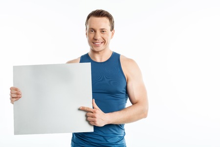 Cheerful man is holding empty blank in his hands. He is pointing at it with his index finger. The man is smiling happily. Isolated on background and copy space in right sideの写真素材
