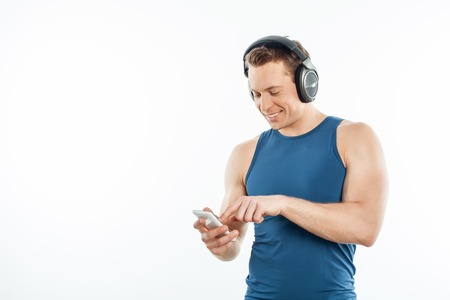 Attractive man is listening to music from headphones. He is holding mobile phone and smiling. The man is choosing music. Isolated on background and copy space in left sideの写真素材