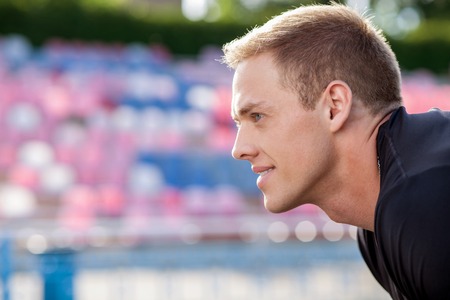 Cheerful young runner is satisfied by his training. He is smiling and looking forward. He is standing in profile. There is copy space in left sideの写真素材