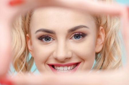 Close up of beautiful woman making frame by her hands. She is looking through it and smilingの写真素材