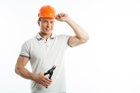 Handsome builder with helmet on his head is holding shears for cutting metal. He is touching his helmet with his hand. The man is smiling. Isolated on background and copy space in right sideの写真素材