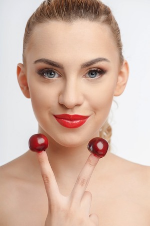 Beautiful woman is showing peace sign. She is smiling gently. Two tasty cherries are situated on her fingers. Isolated on backgroundの写真素材
