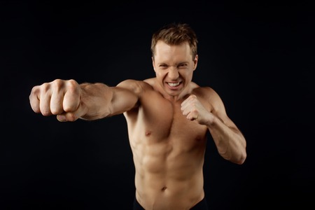 Attractive sportsman is fighting with his fist raised. He is looking forward with aggression. Isolated on black backgroundの写真素材