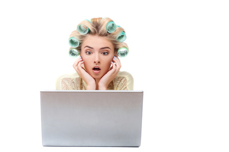 Beautiful housewife is sitting near small computer. She is looking at it with shock. Her mouth and eyes are wide open. Isolated on background and copy space in right sideの写真素材