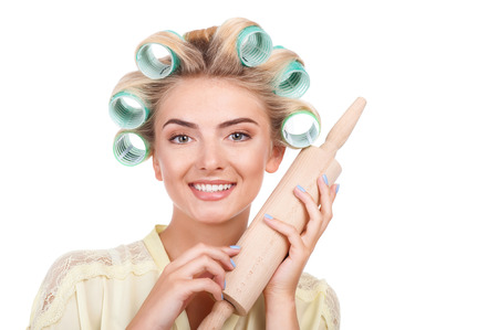 Beautiful housewife is holding rolling pin near her face. She is smiling and looking at the camera with happiness. Isolated on background and copy space in right sideの写真素材