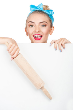 Beautiful girl is peeping through horizontal wall. She is holding rolling-pin and smiling. Isolated on backgroundの写真素材