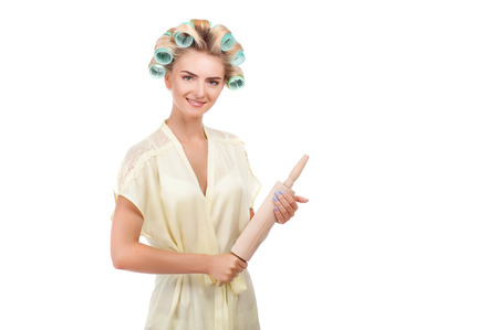 Beautiful housewife is holding rolling pin. She is looking at the camera with threatens and smiling. Isolated on background and there is copy space in right sideの写真素材