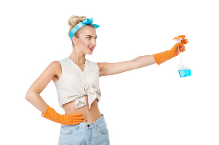 Attractive young woman is stretching her hand with cleaning spray aside. She is smiling and looking at it with interest. The girl is wearing rubber gloves. Isolated on backgroundの写真素材