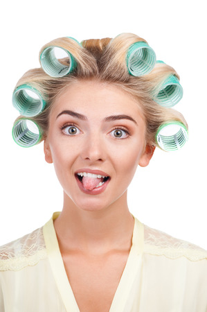 Cheerful woman is showing her tongue with irony. She has blue curlers in her hair. Isolated on backgroundの写真素材