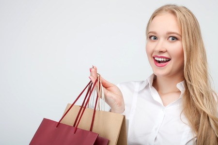 Beautiful young blond woman wants to buy everything. She is looking forward with passion and laughing. The girl is holding packets with desire. Isolated on backgroundの写真素材