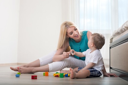 Beautiful mom is spending time with her baby in bedroom. They play with toys. The parent and her chills are looking at each other and smilingの写真素材