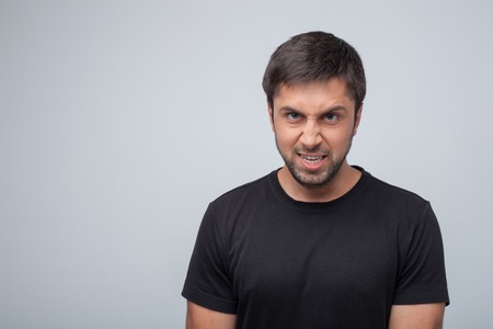 Frustrated violent guy is expressing his anger. He is showing his teeth dangerously. Isolated on grey background and copy space in left sideの写真素材